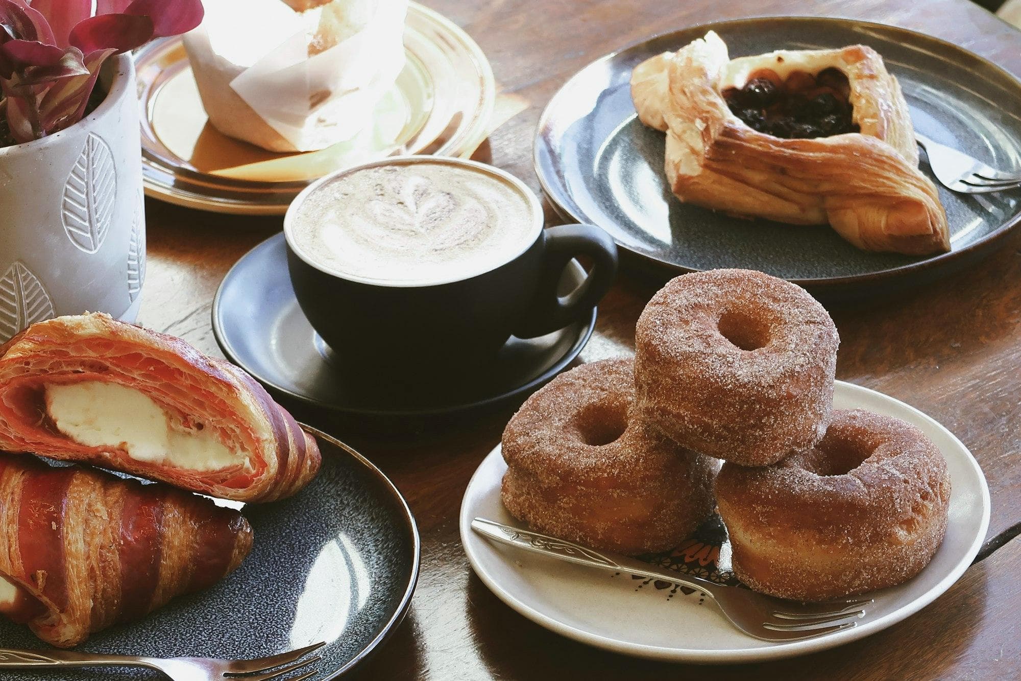 A latte with croissants, a fruit danish and cinnamon doughnuts on a timber café table in Canberra