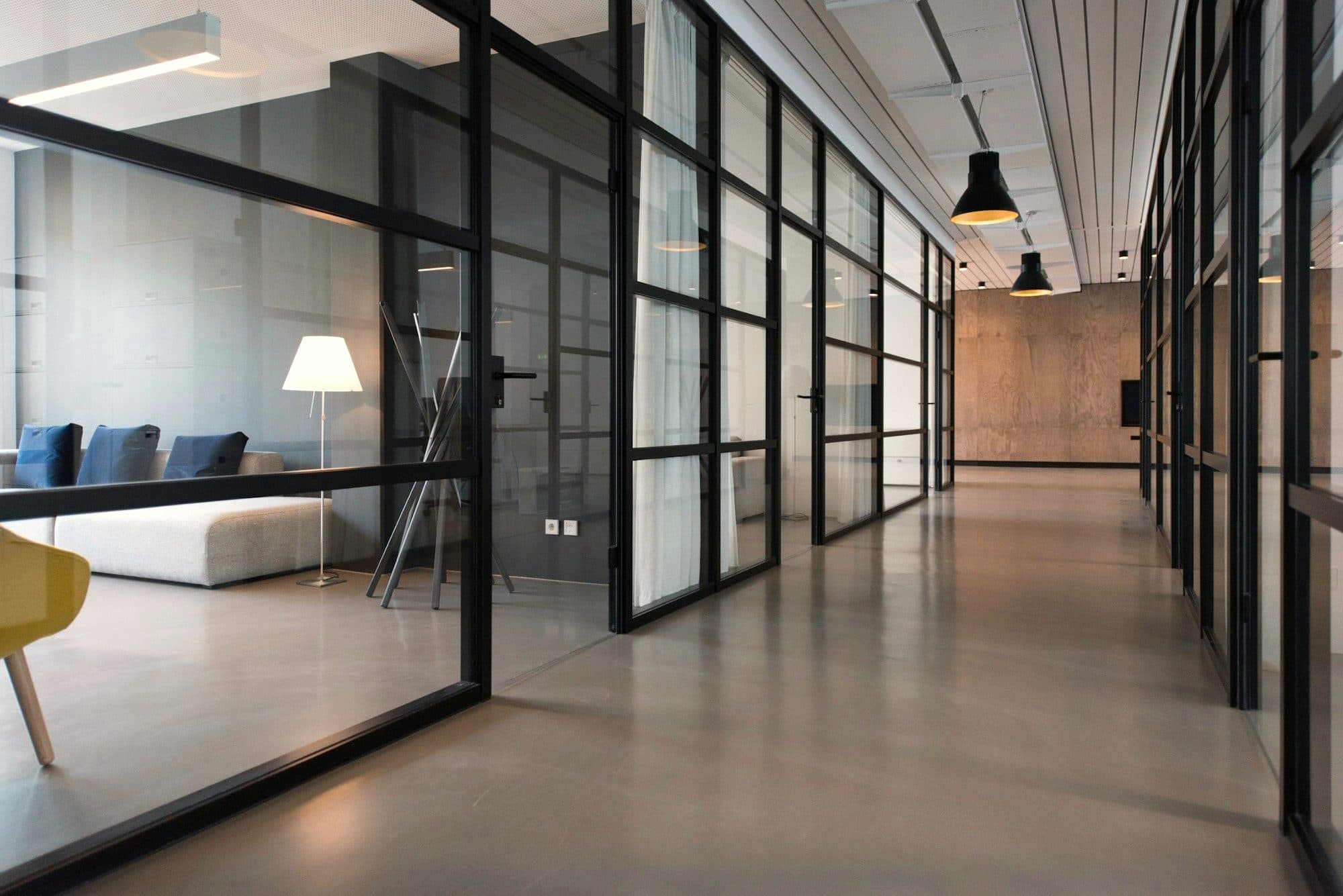 A quiet office corridor lined with glass-walled private rooms and soft pendant lights
