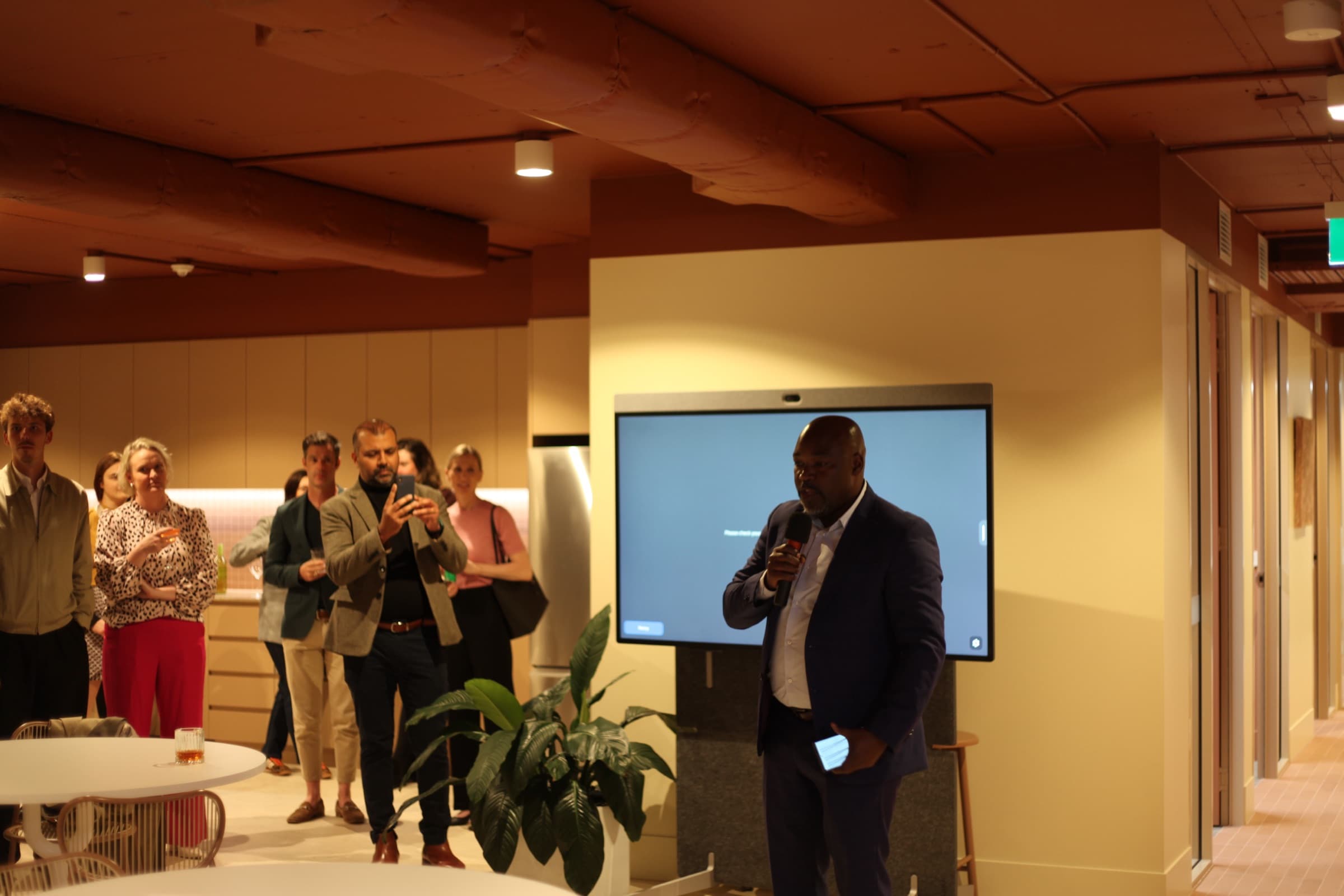 A host welcoming guests in front of a screen
