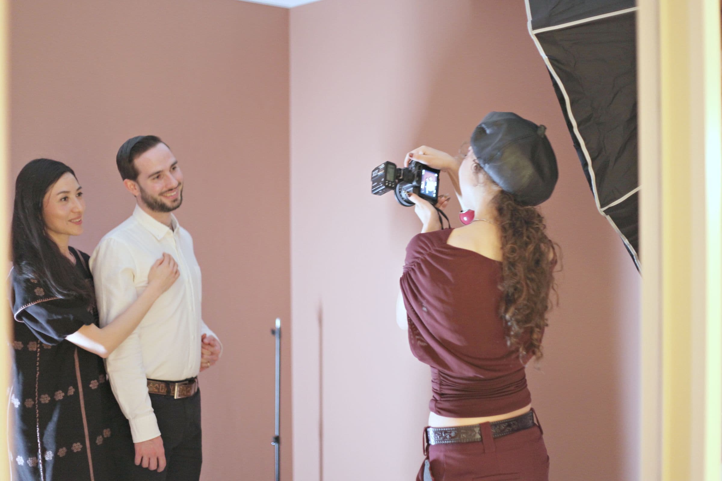 A photographer shooting two people against a pink wall, with a softbox light to the side